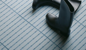 Detaljbilde av gulv med blå, små gulvfliser og støvler som er slengt